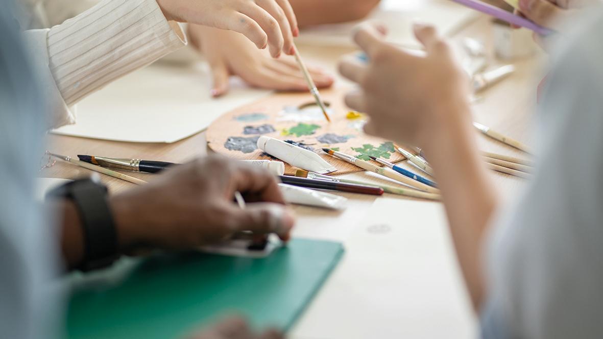 Hände, Zeichen- und Malerwerkzeuge auf dem Tisch