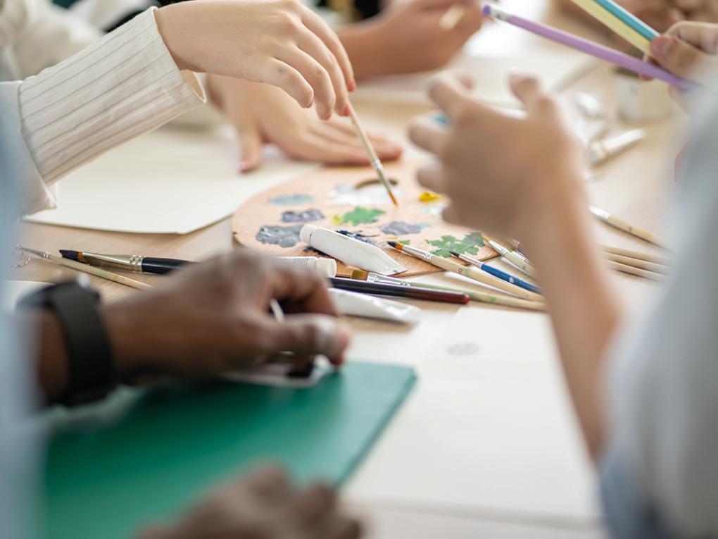 Hände, Zeichen- und Malerwerkzeuge auf dem Tisch