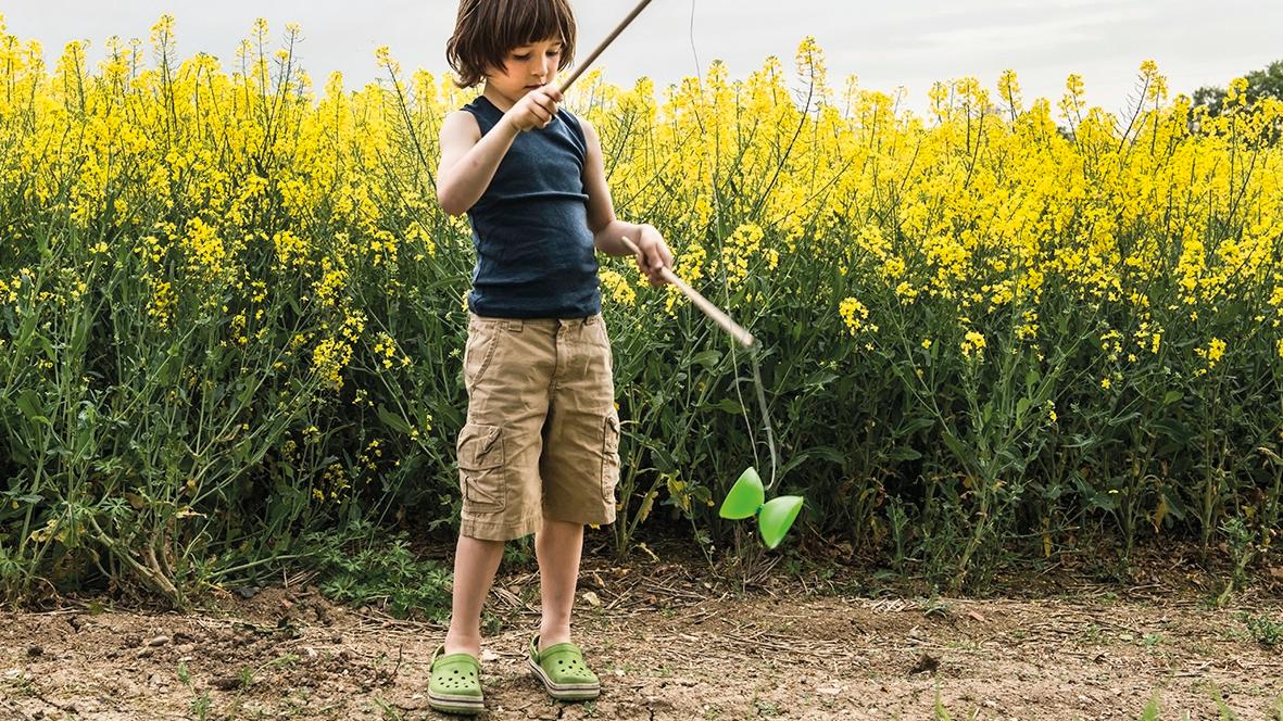 Junge spielt in einem gelben Blumenfeld mit einem Diabolo