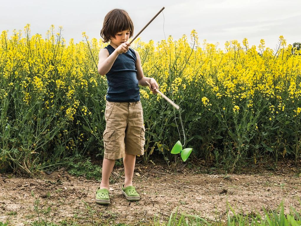 Junge spielt in einem gelben Blumenfeld mit einem Diabolo